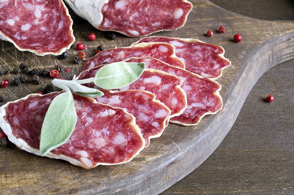 slices of french cheese dried salami with spices on wooden background
